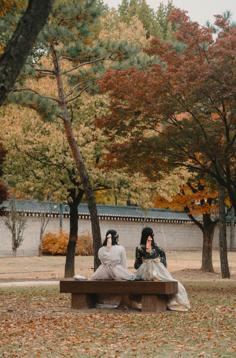 Two Women Sitting Next To Each Other in Autumn-like Weather